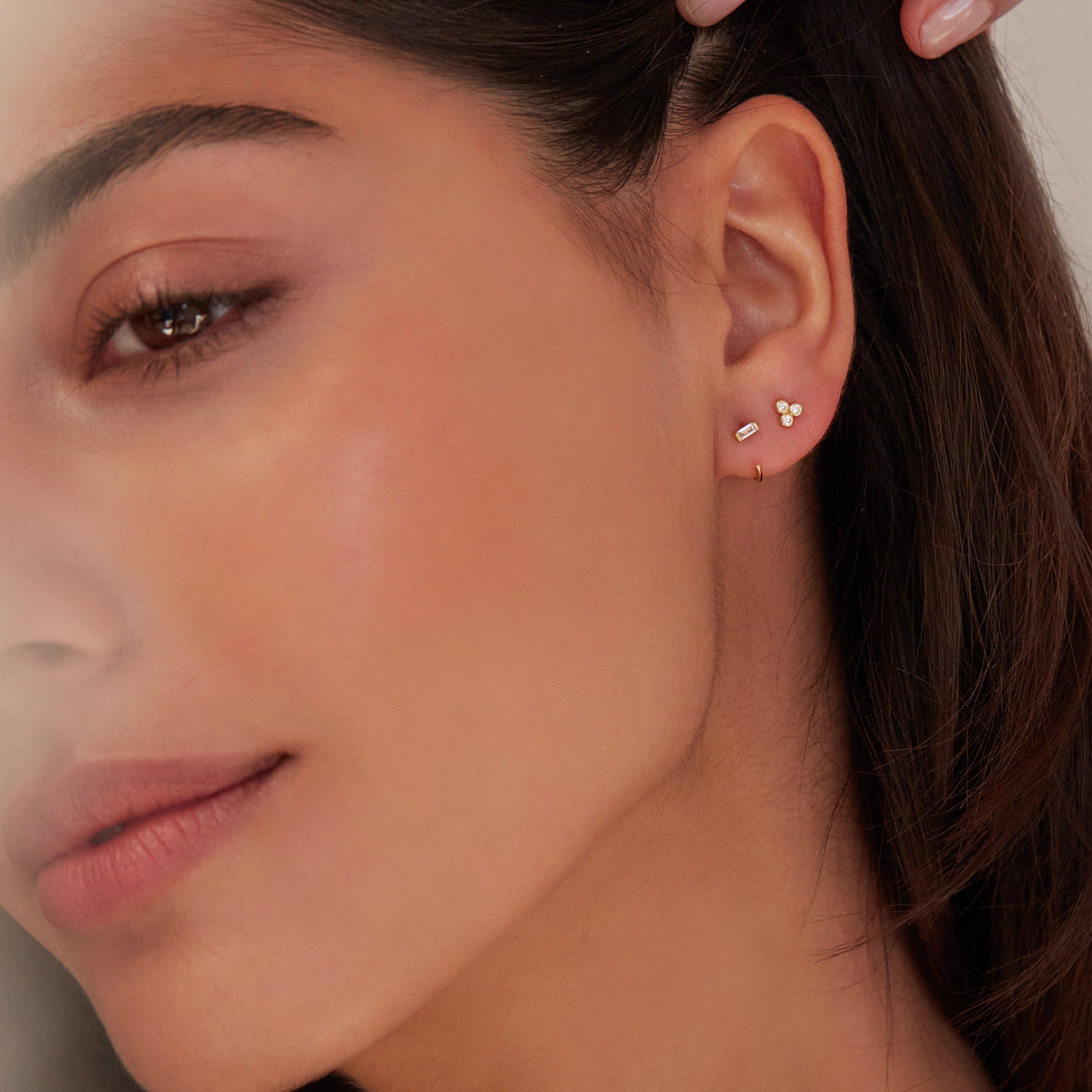 Silver diamond style baguette lobe hoop earring and a gold diamond style pyramid stud earring in one ear lobe close up