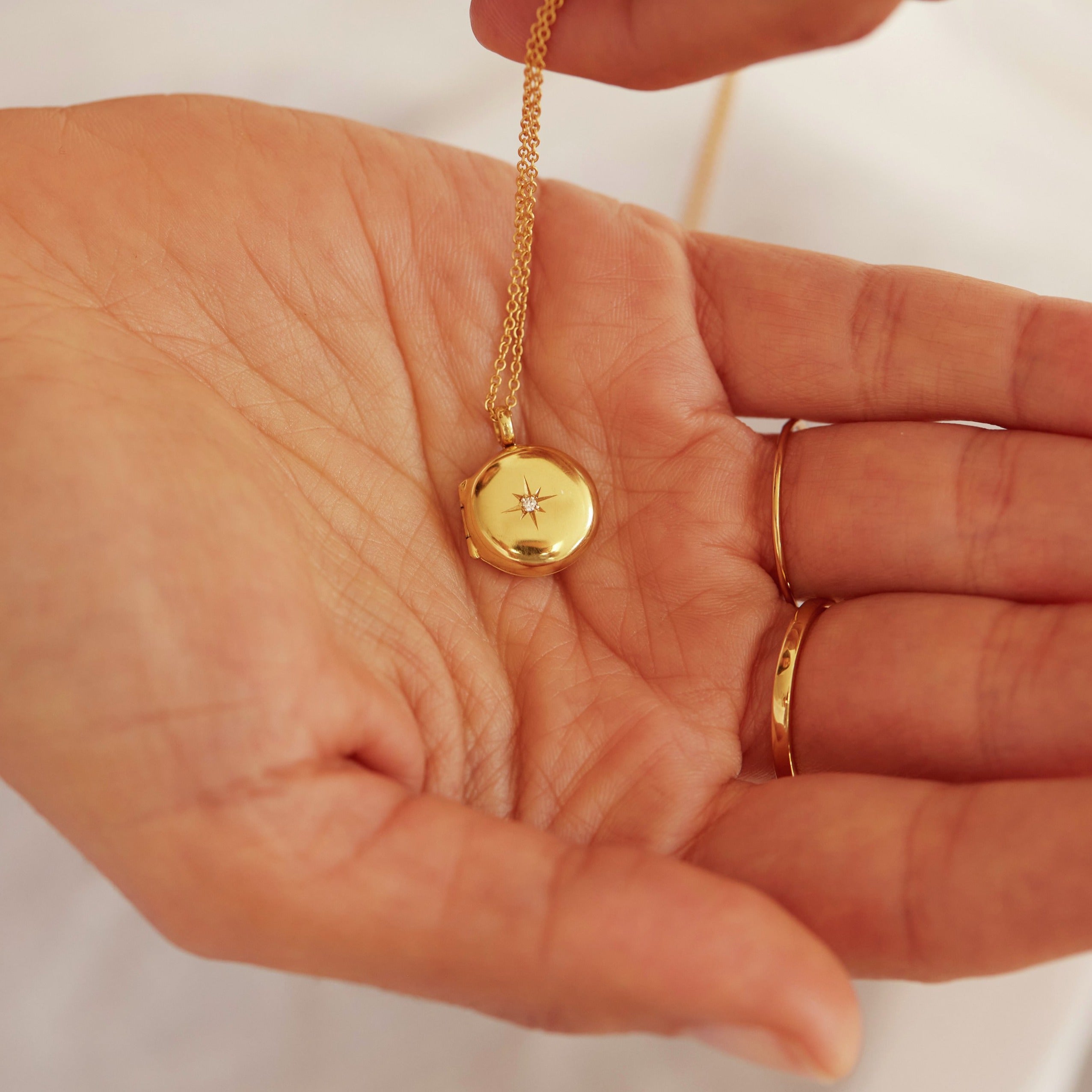 A gold small round diamond locket necklace in the palm of a woman's hand