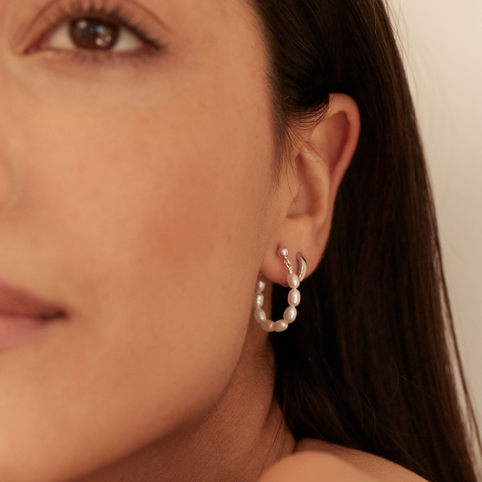 Silver seed pearl hoop earring in an ear lobe close up, paired with a silver huggie hoop earring
