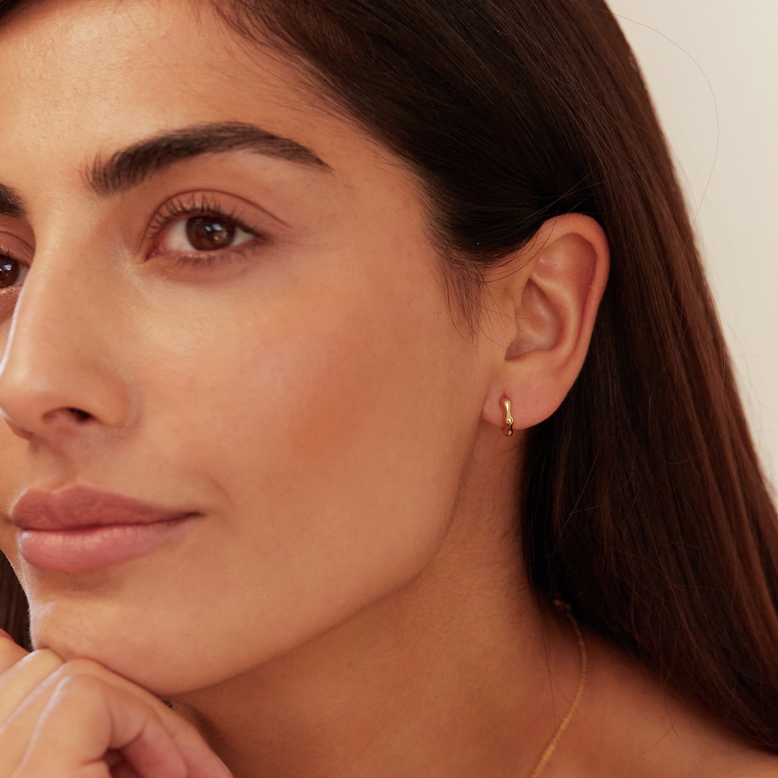 Gold molten huggie hoop earring in one ear lobe of a brunette woman with brown eyes