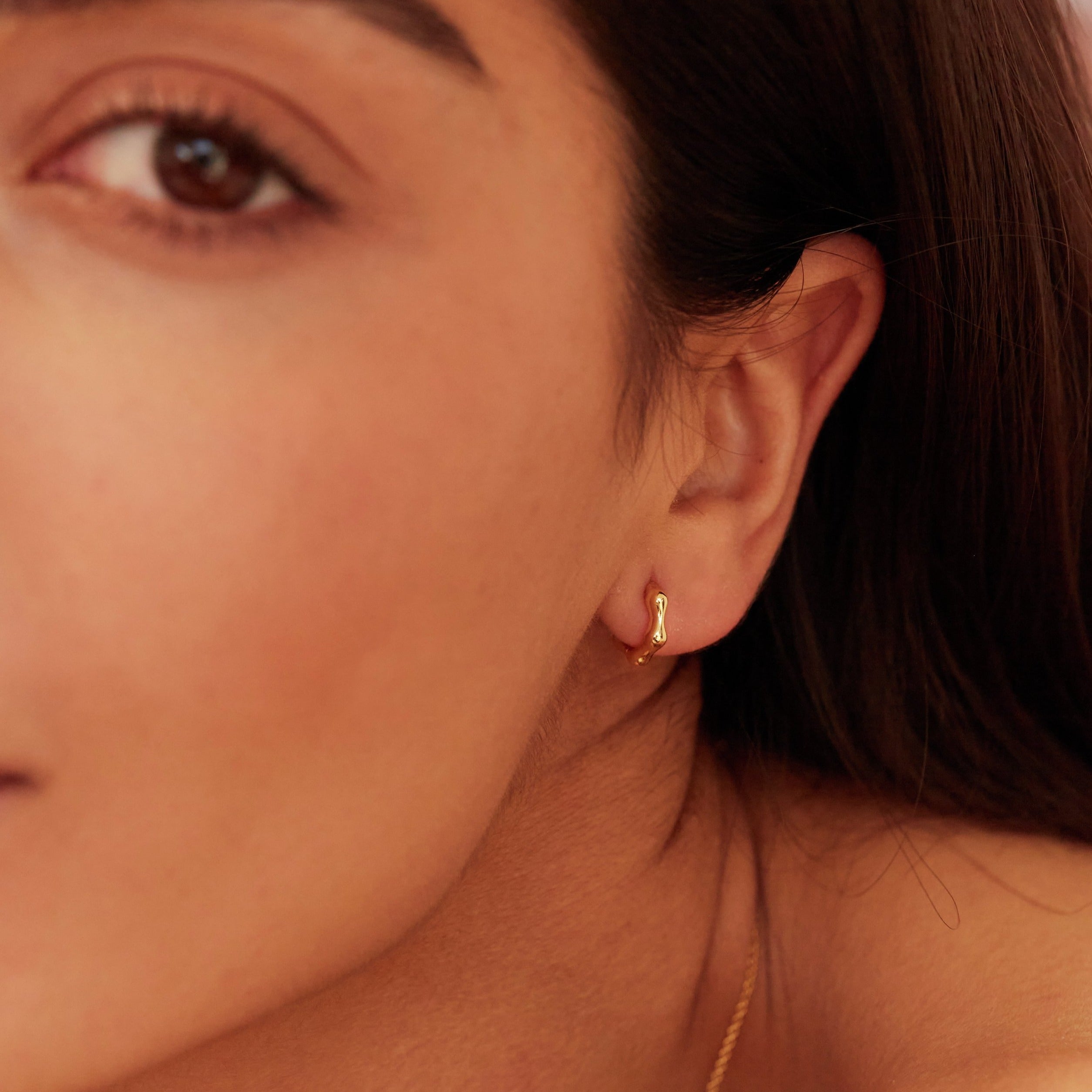 Gold molten huggie hoop earring in one ear lobe