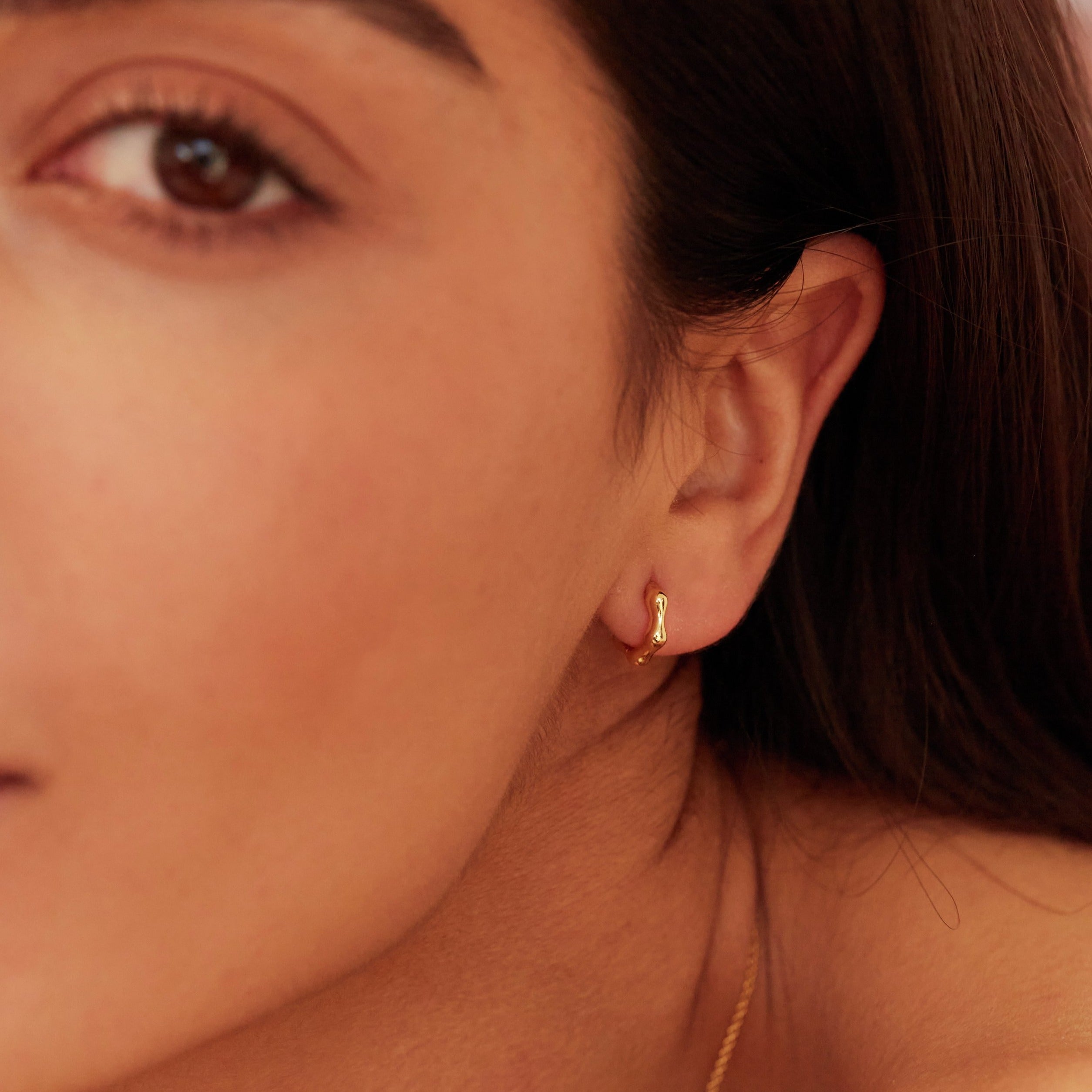 Gold molten huggie hoop earring in one ear lobe