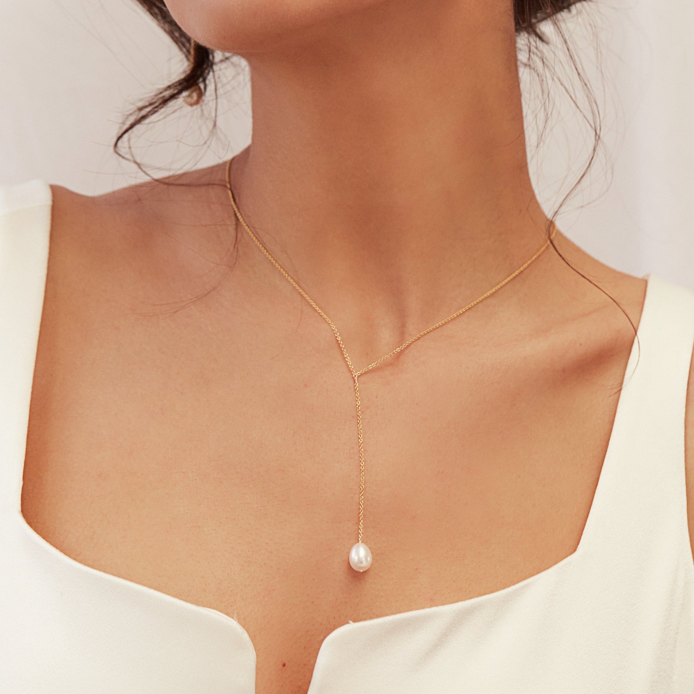 Gold large pearl lariat necklace around a neck with head to the slide