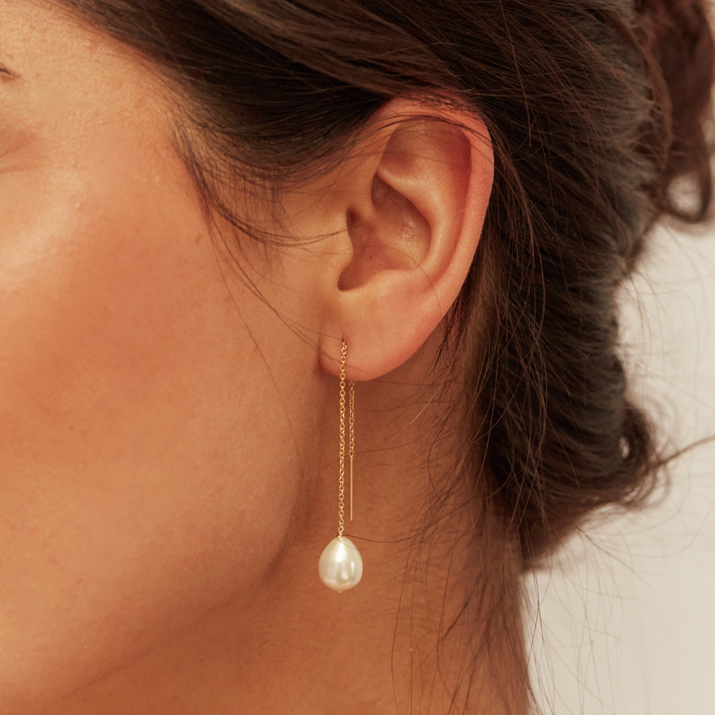Gold large pearl drop ear threader in one ear lobe of a brunette woman with her hair up