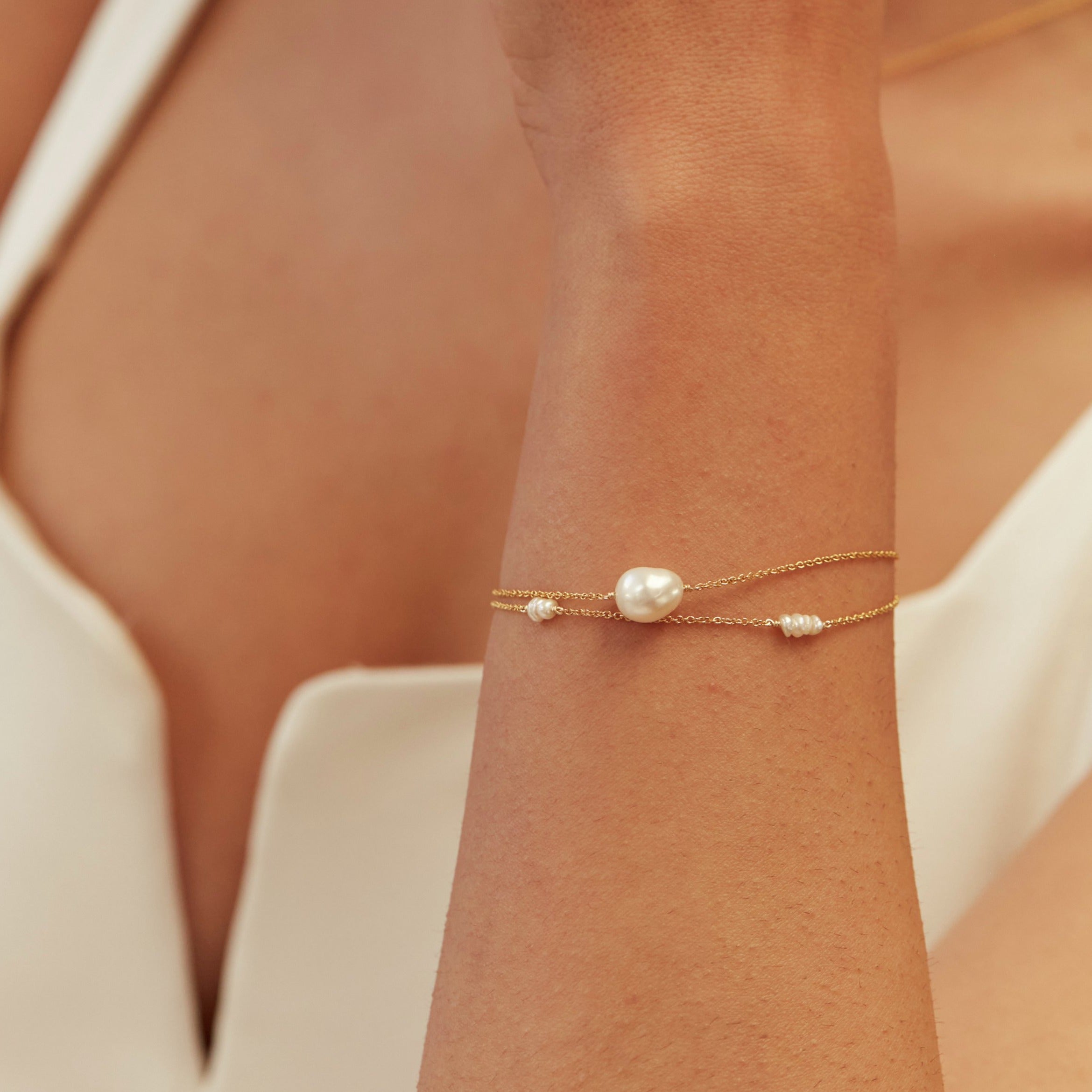 Gold mini pearl bracelet on a wrist held over chest