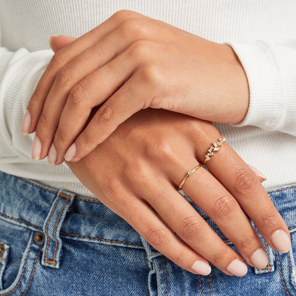 A gold diamond style baguette ring on a finger with gold thin diamond style stacking ring on the other finger