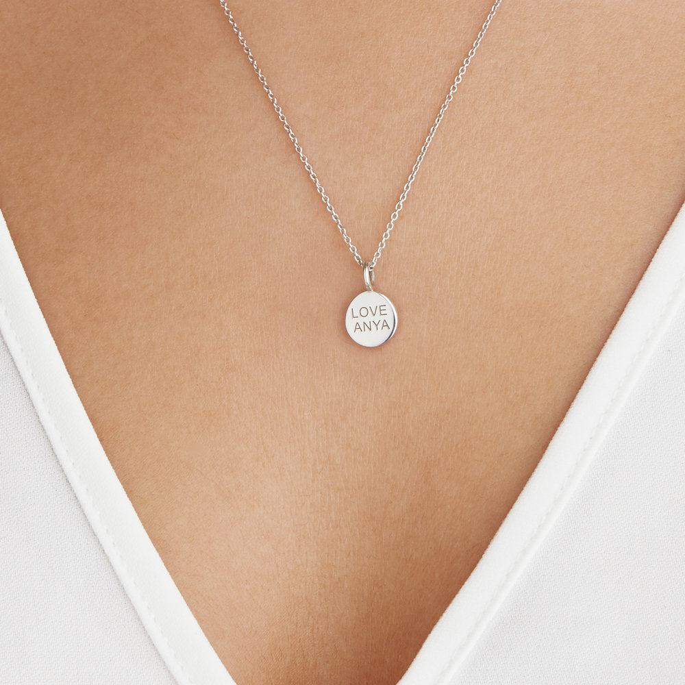 Silver small personalised disc necklace with 'LOVE ANYA' engraved on a woman's chest 