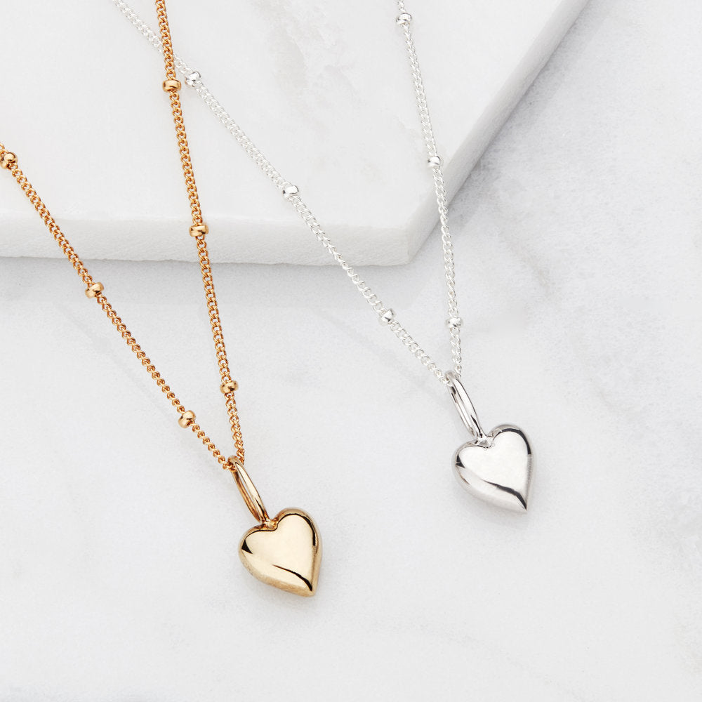 Gold heart pendant necklace and silver heart pendant necklace on marble surfaces