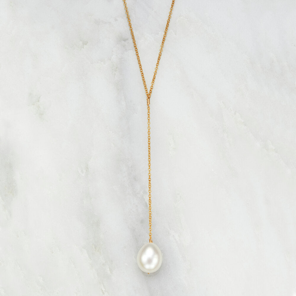 Gold large pearl lariat necklace on a marble background