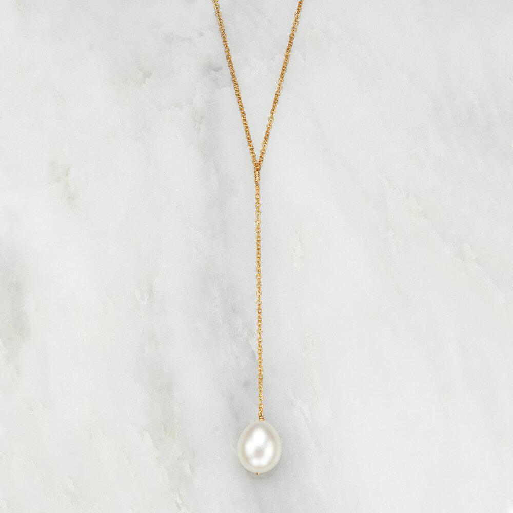 Gold large pearl lariat necklace on a marble background