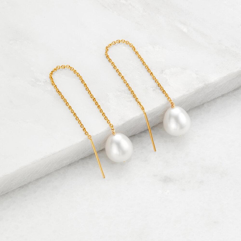Gold large pearl drop ear threaders on marble surfaces