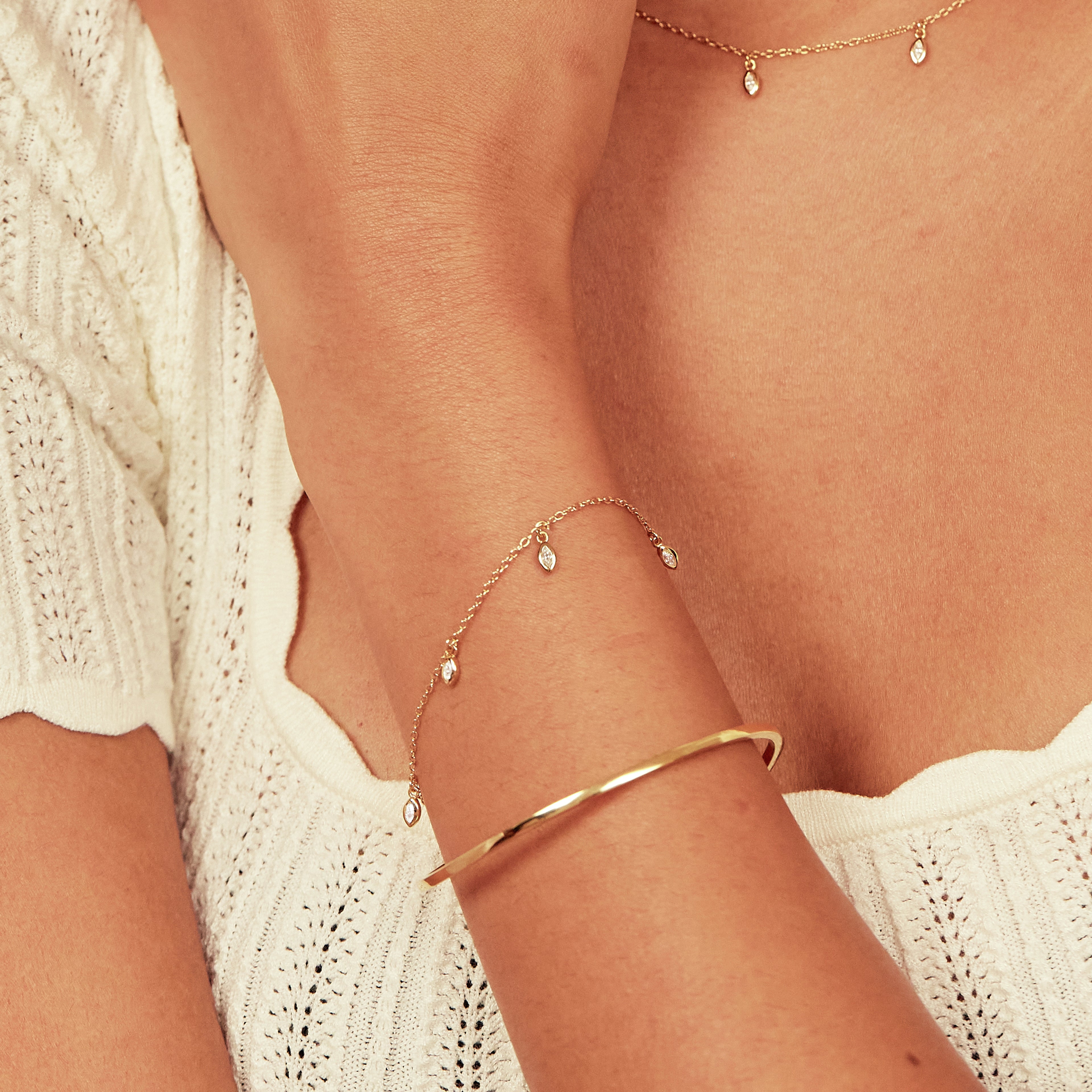 Gold diamond style marquise drop bracelet around a wrist layered with a gold bangle and with a gold diamond style marquise drop necklace around the neck