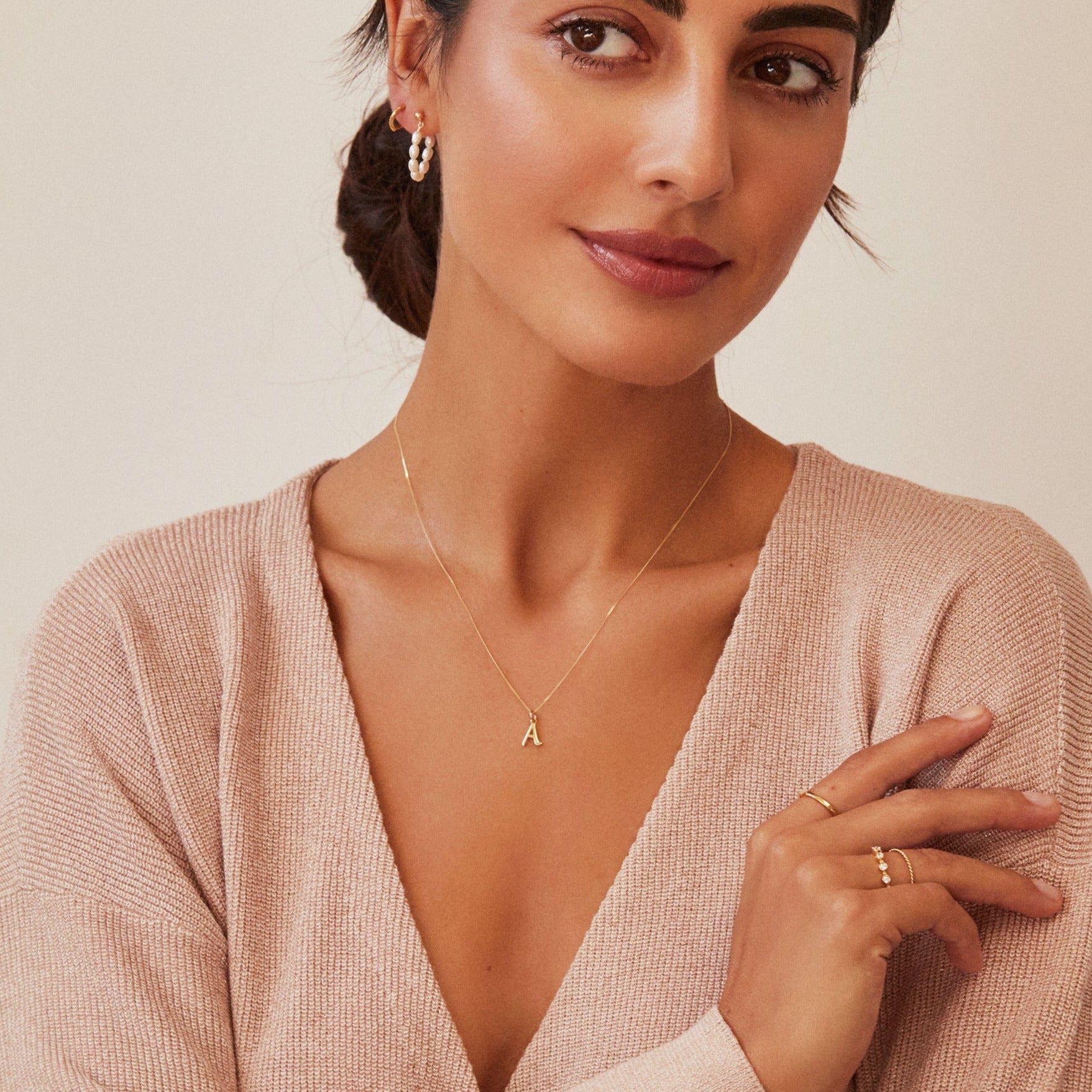 Gold seed pearl hoop earring in ear lobe of a dark haired woman looking to the side with a silver individual curve initial charm 'A' around her neck