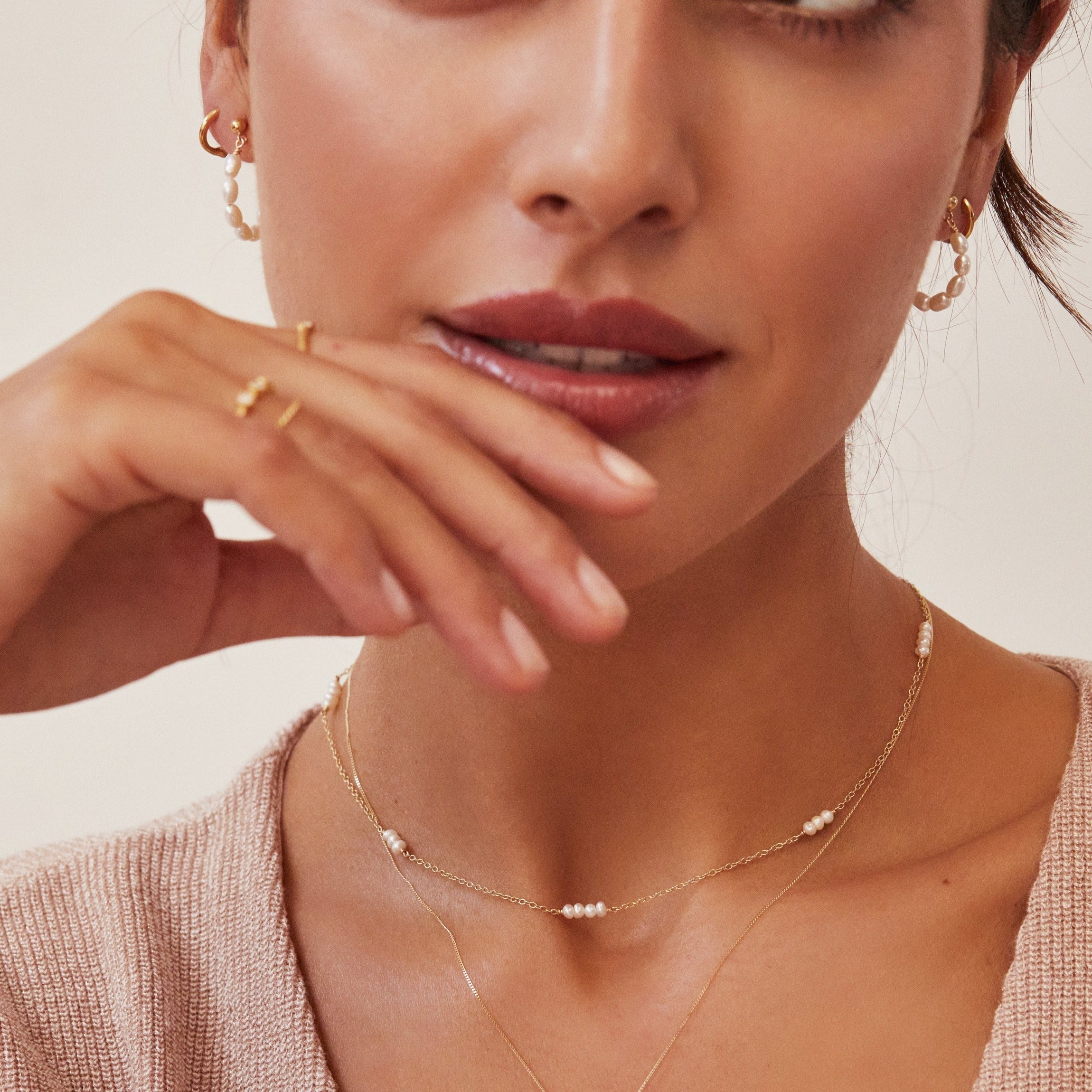 Gold mini pearl choker on brunette woman with two fingers to her lips