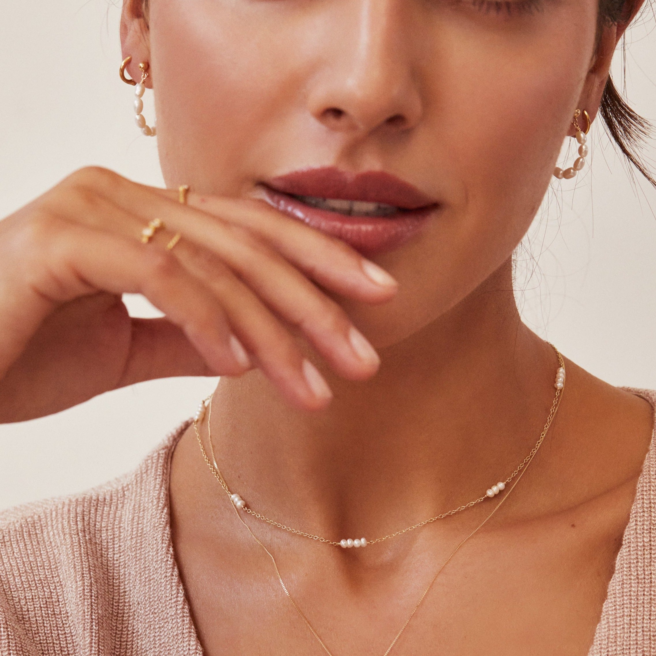 Gold mini pearl choker on brunette woman with two fingers to her lips