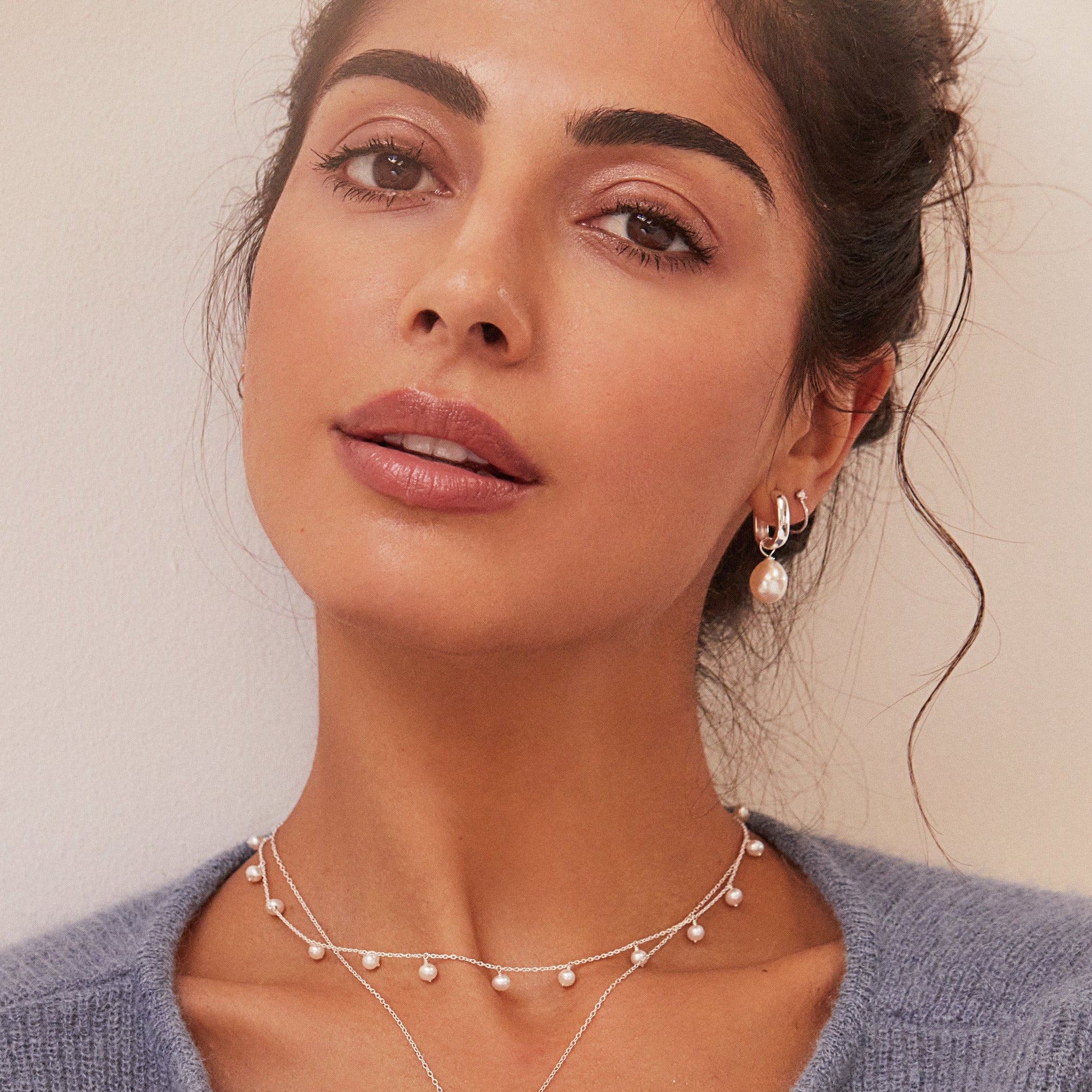 Silver thick squared hoop pearl drop earring an ear lobe of a woman wearing a silver drop pearl choker around her neck