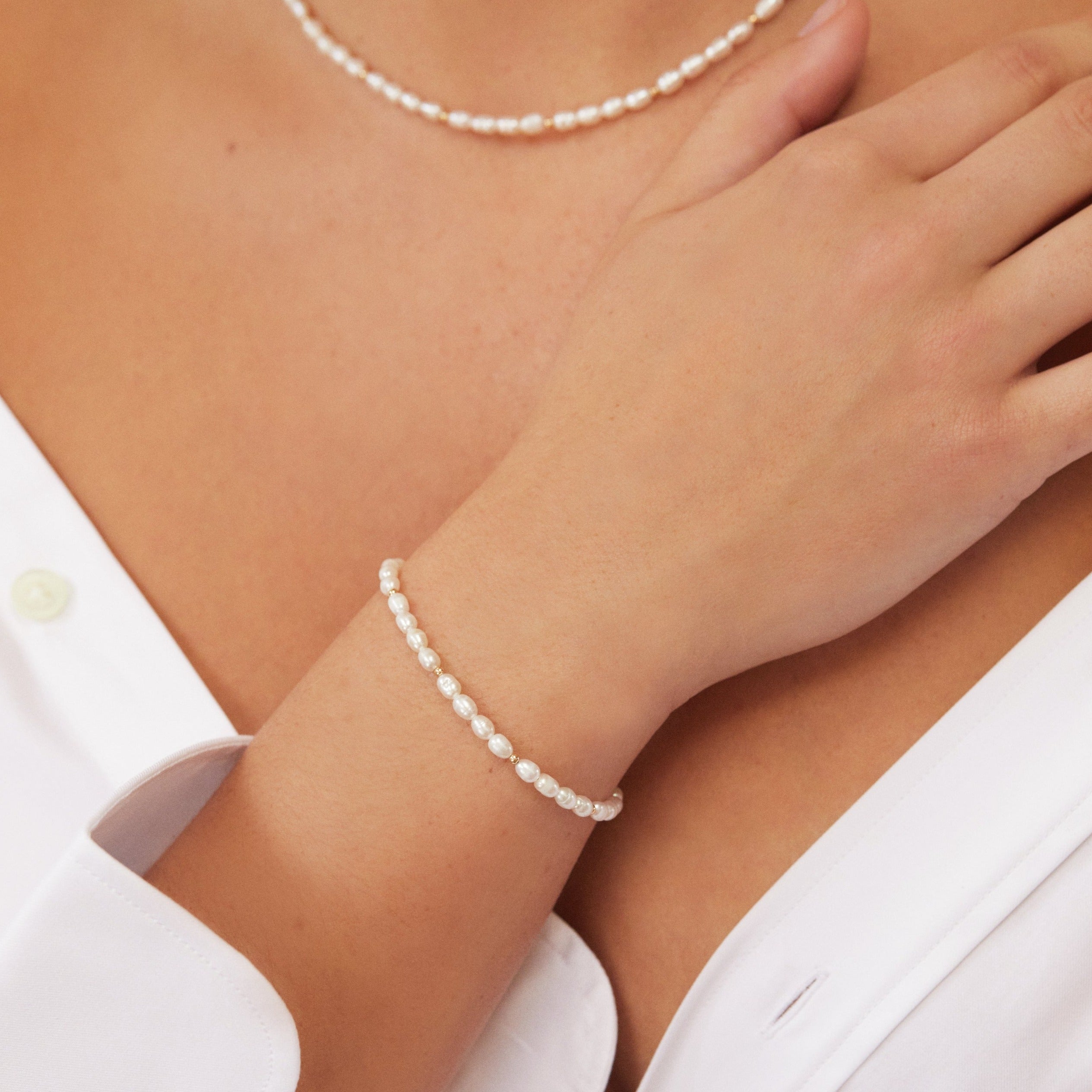 Gold beaded seed pearl bracelet on a wrist with matching necklace around the neck