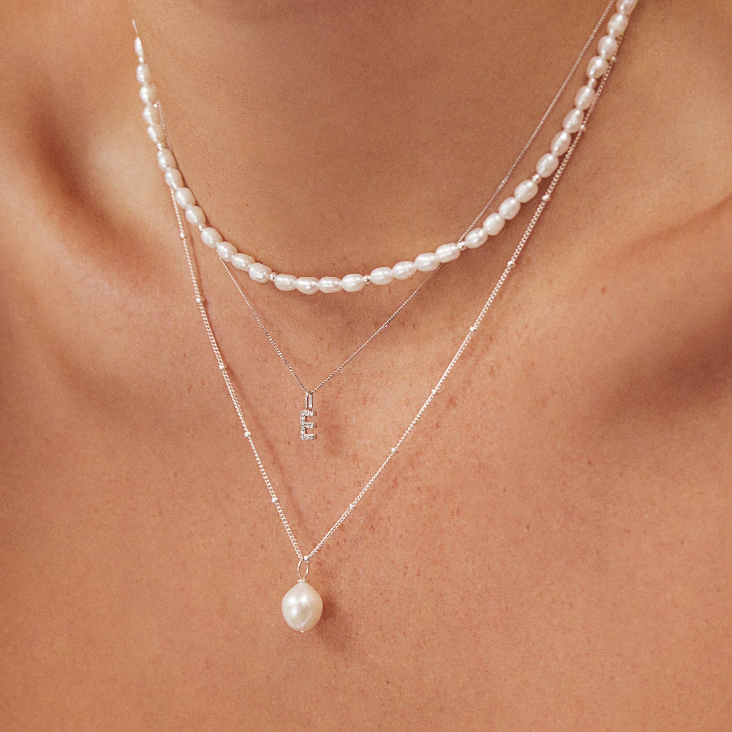 Silver beaded seed pearl choker layered with a silver 'E' letter necklace and a silver satelite single pearl choker around a neck