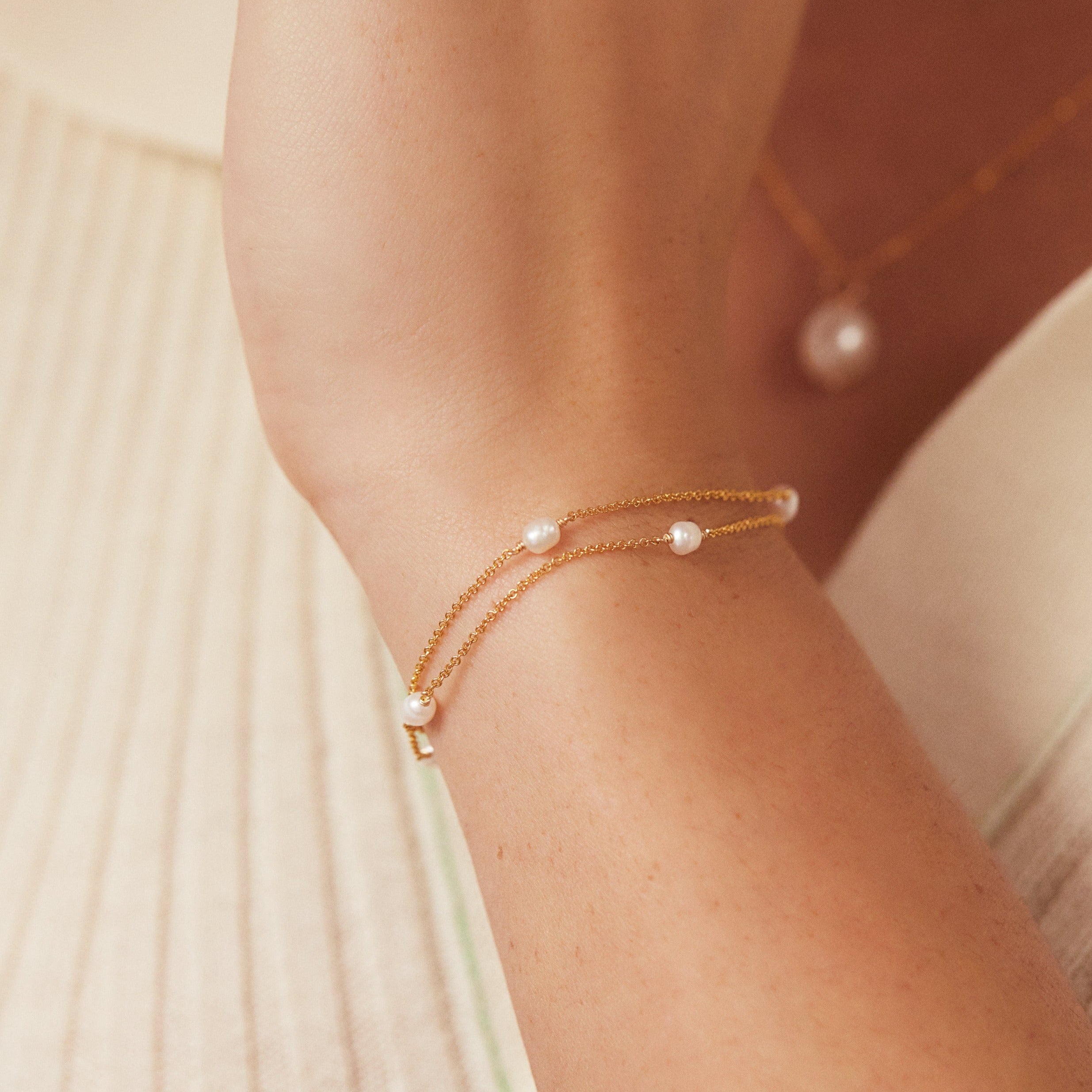 Gold layered seed pearl bracelet on wrist infront of chest faded in the background