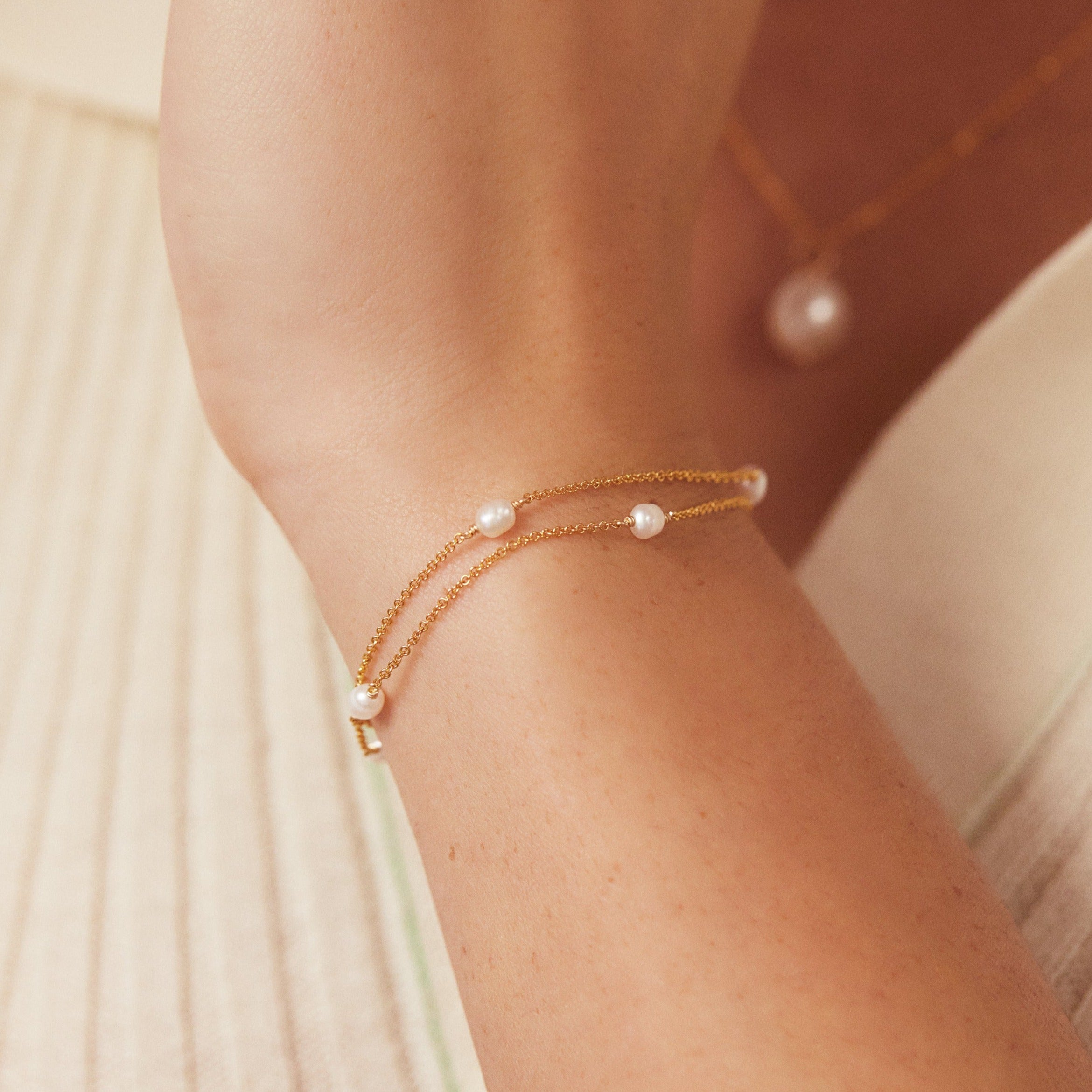 Gold layered seed pearl bracelet on wrist infront of chest faded in the background