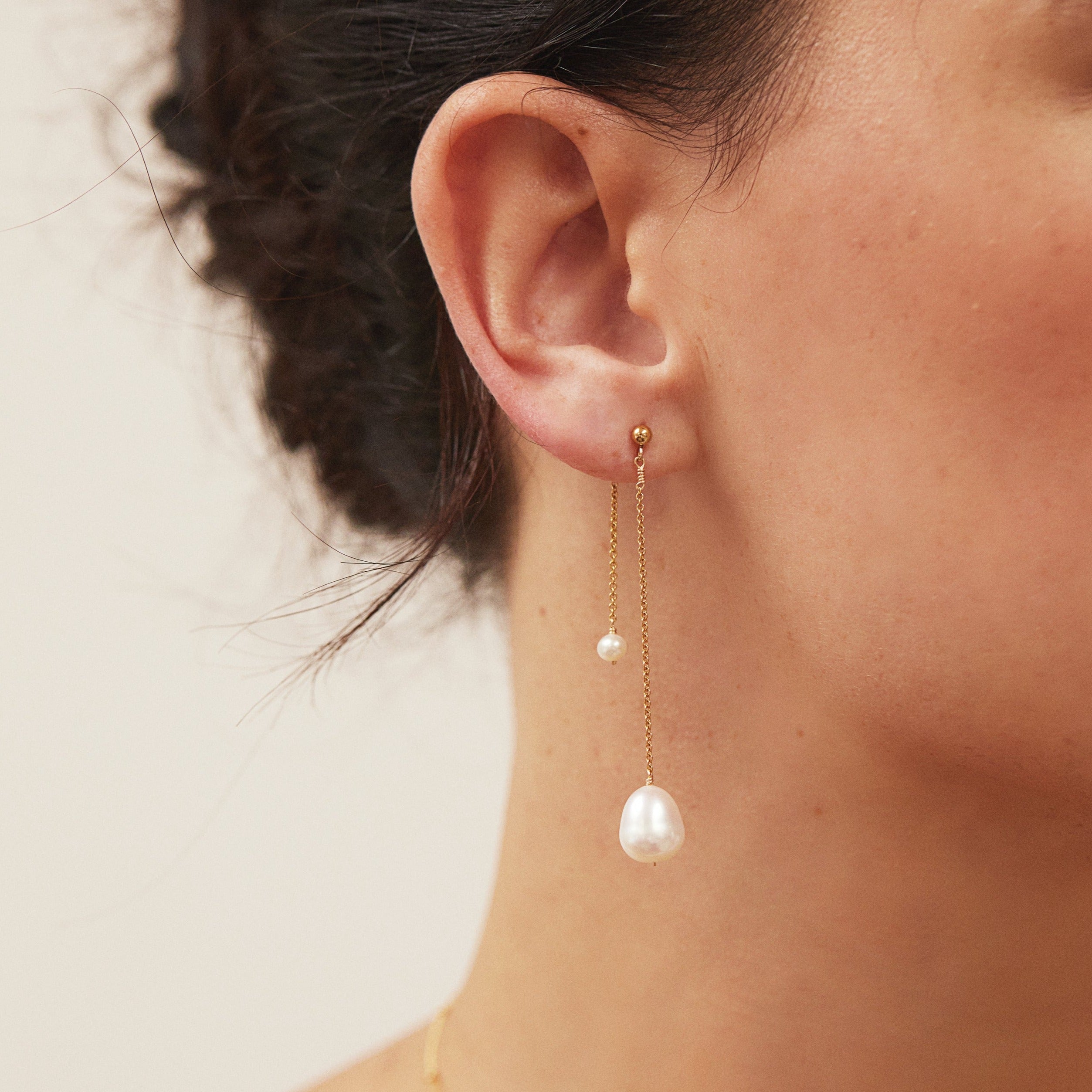 Gold layered large and small pearl earring in one ear lobe of a brunette woman