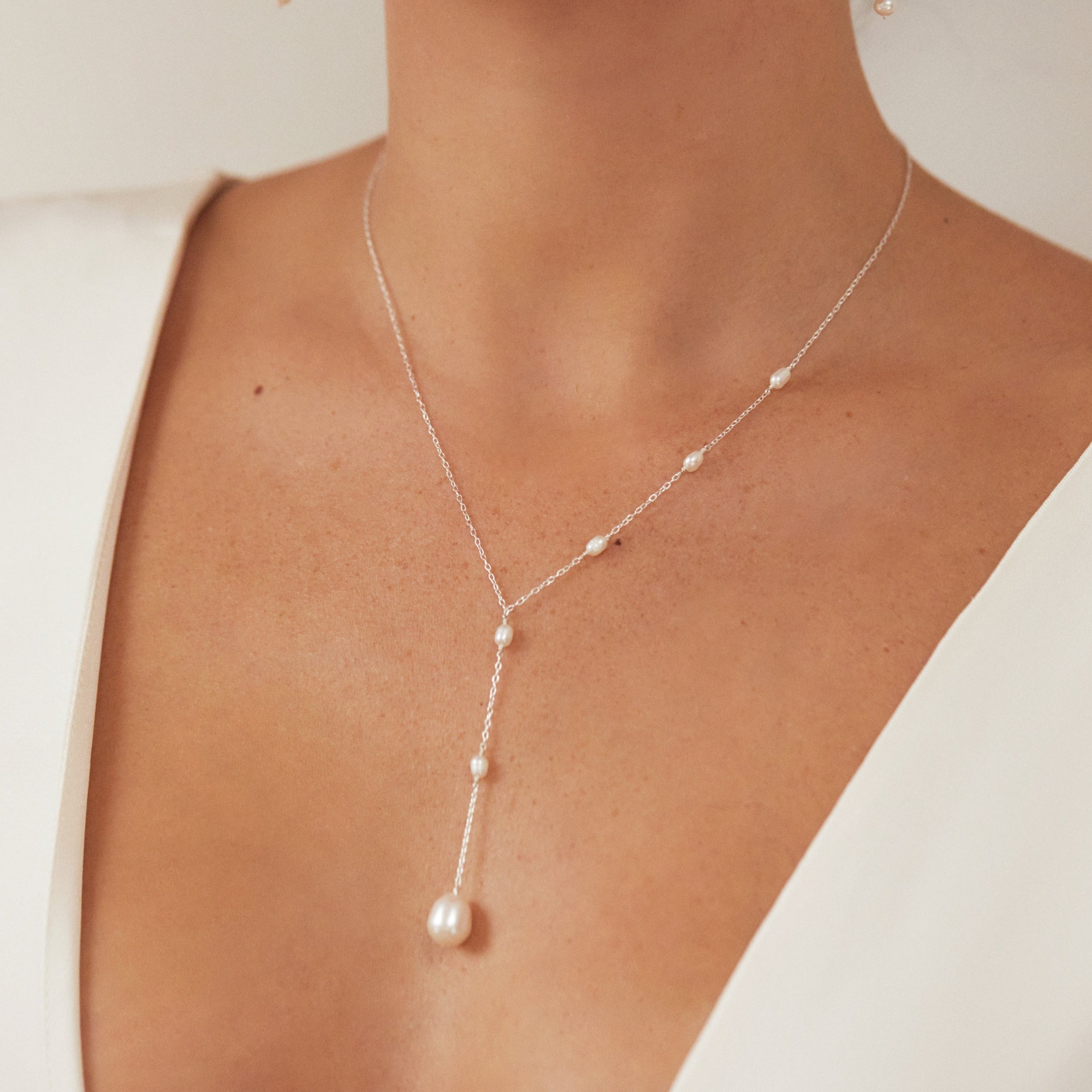 Silver seed pearl lariat necklace on chest around a neck