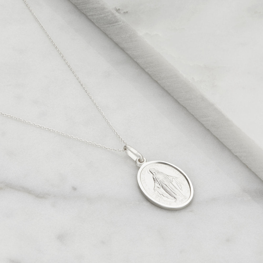 Silver small virgin mary necklace on a marble surface