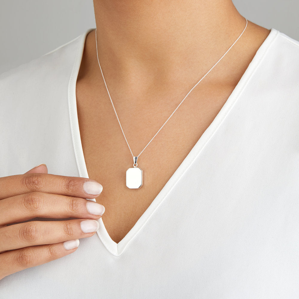 Silver small square locket necklace around a neck of a woman wearing a white V-neck top