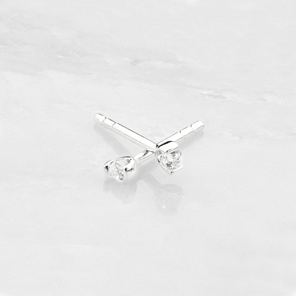 Silver small diamond style studs crossed over one another on a marble surface