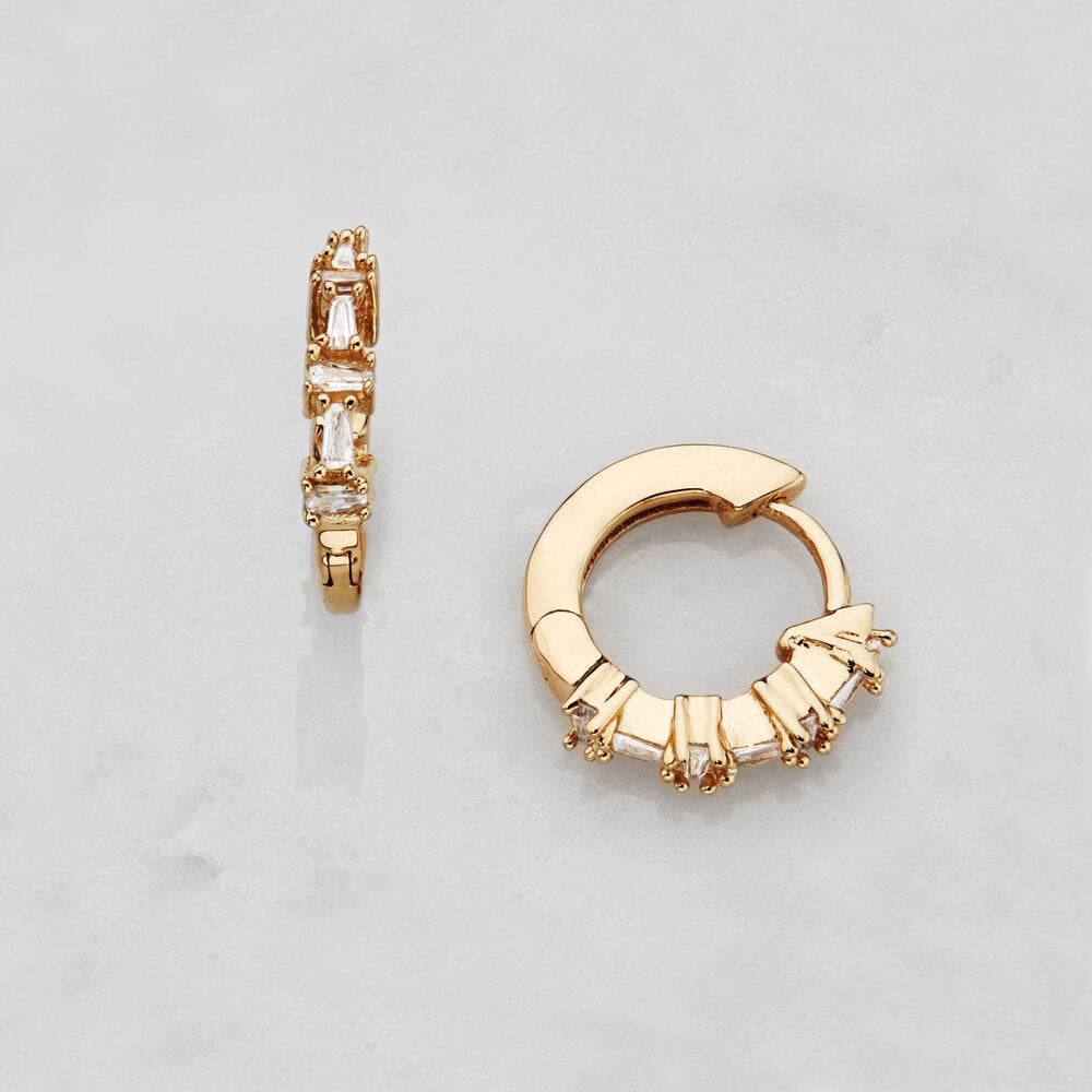 Gold diamond style baguette huggie hoop earrings on a marble surface