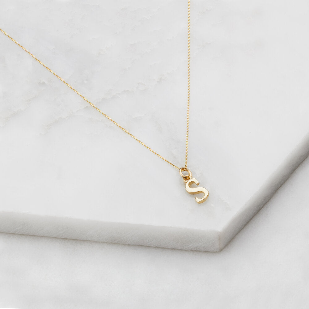 Solid gold curve initial letter necklace 'S' on marble surfaces
