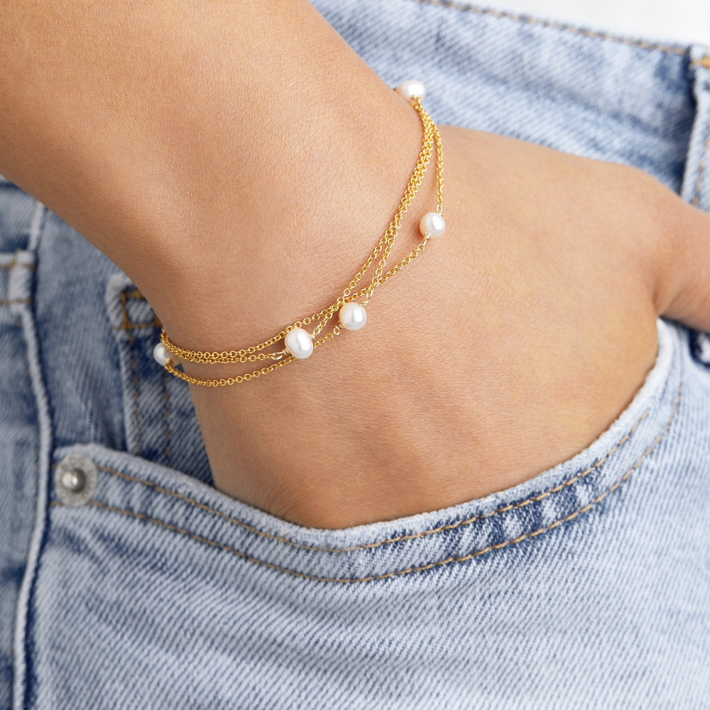 Gold layered pearl bracelet on a wrist with hand in blue jean pocket