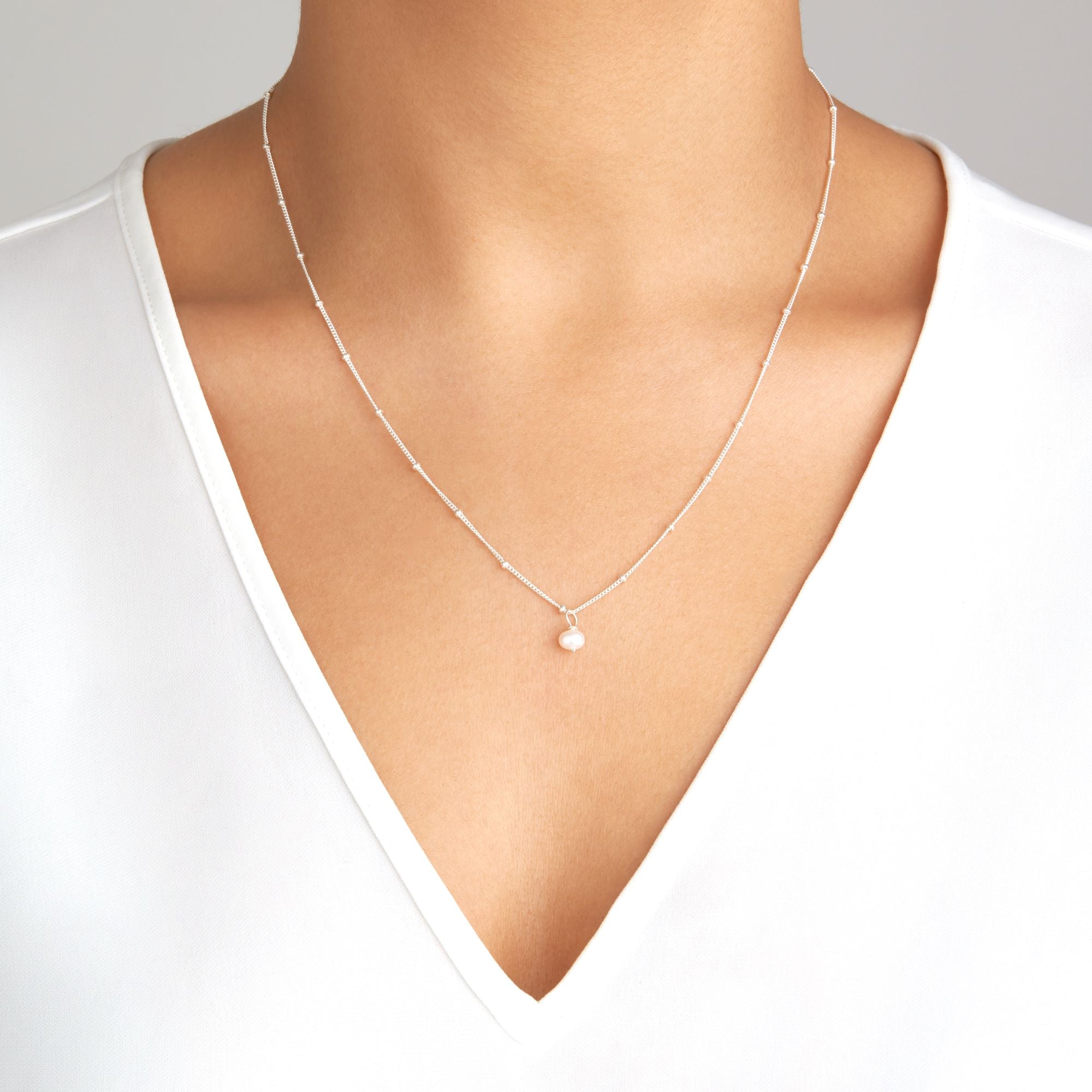 Silver single pearl satellite necklace around a neck of a woman wearing a white V-neck top