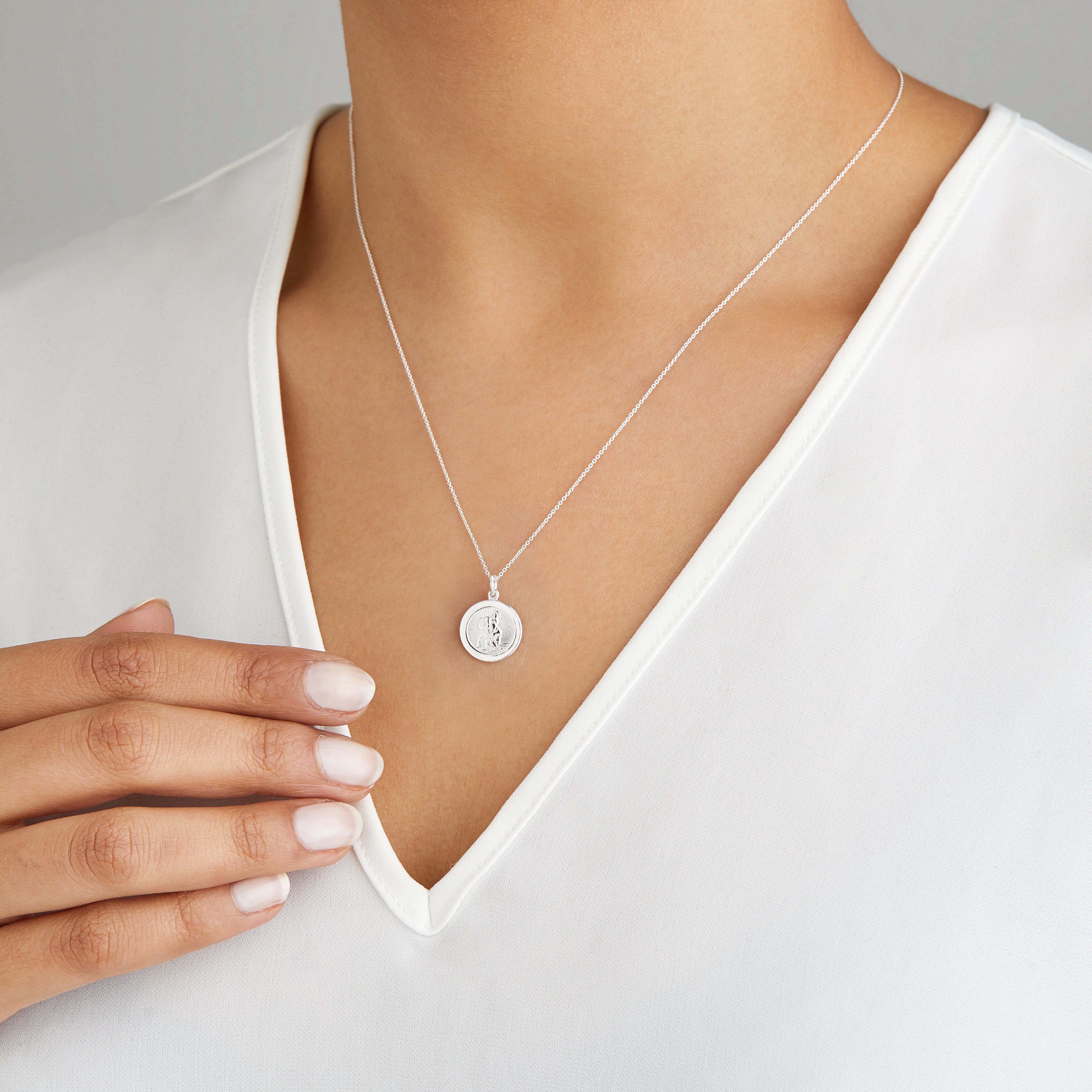 Silver small round St Christopher medallion necklace around teh neck of a woman wearing a white V-neck top