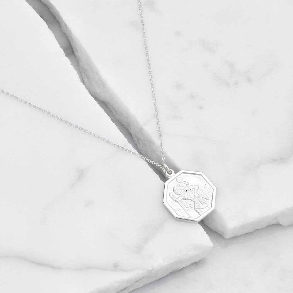 Silver St Christopher octagonal medallion necklace on top of a small gap between two marble blocks