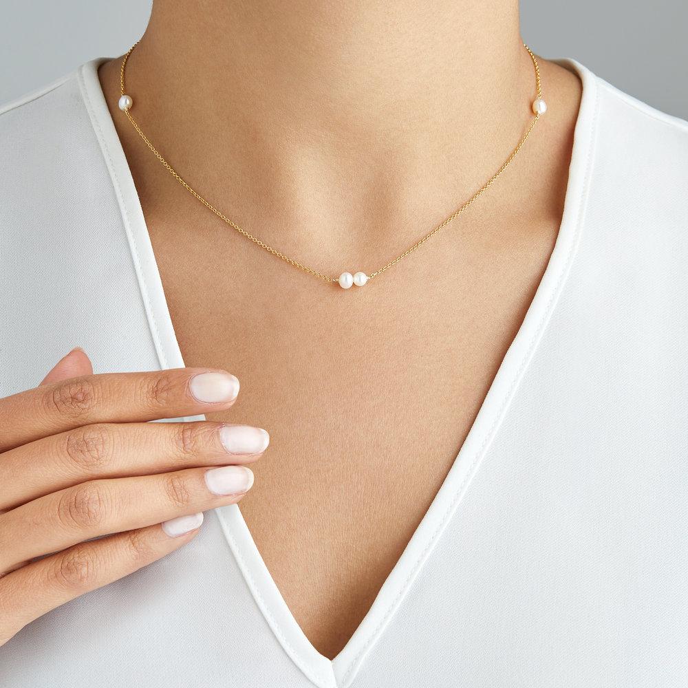 Gold six pearl choker necklace around a neck with a white V neck top
