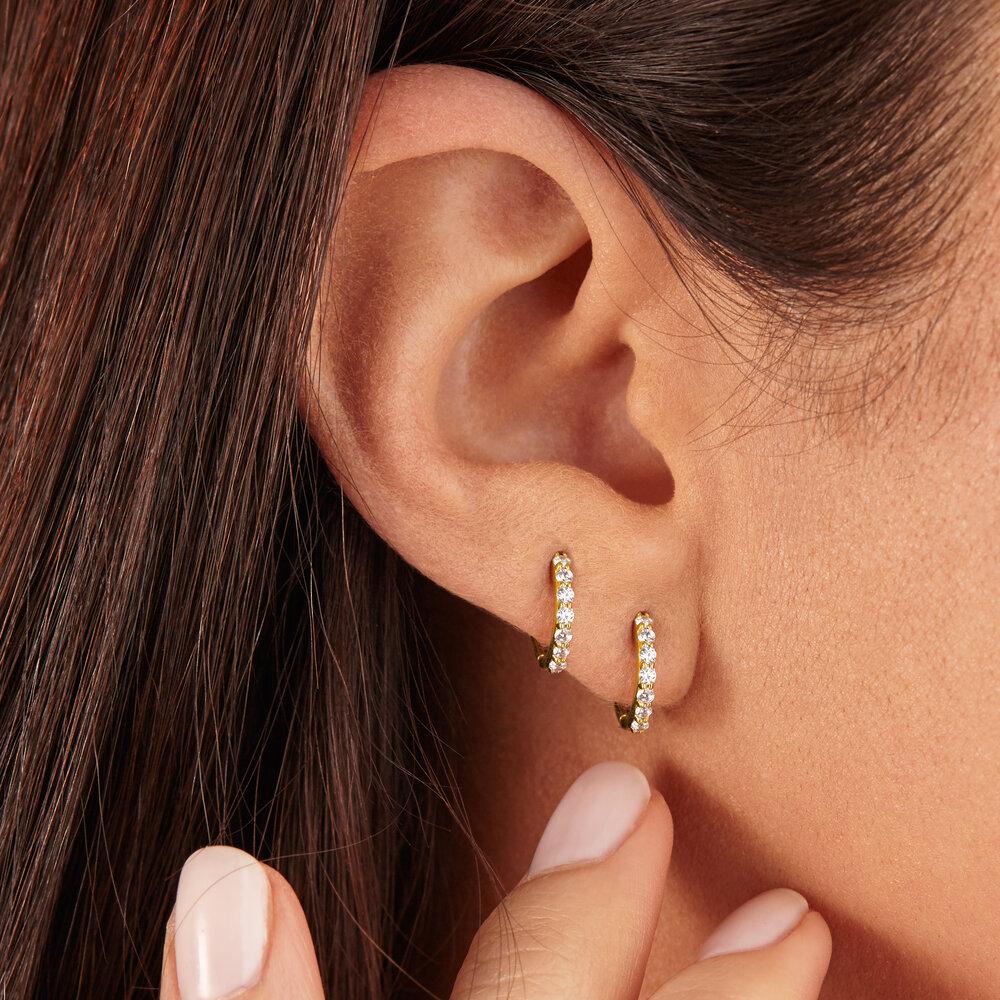 Two gold diamond style huggie hoop earrings in one ear lobe