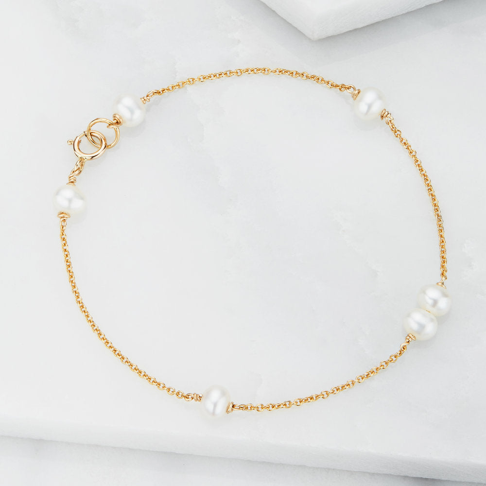 Gold six pearl bracelet lying on a marble surface