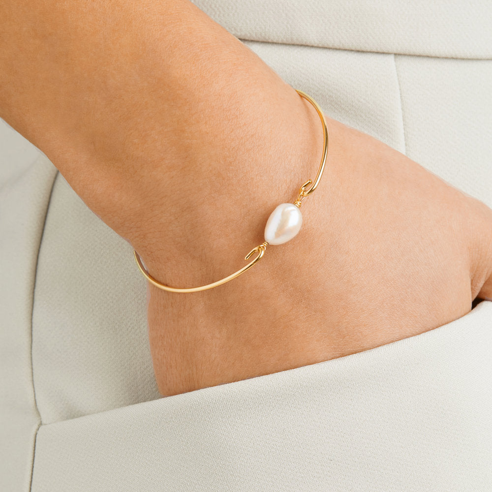 Gold large pearl bangle on a wrist with hand in cream trouser pocket