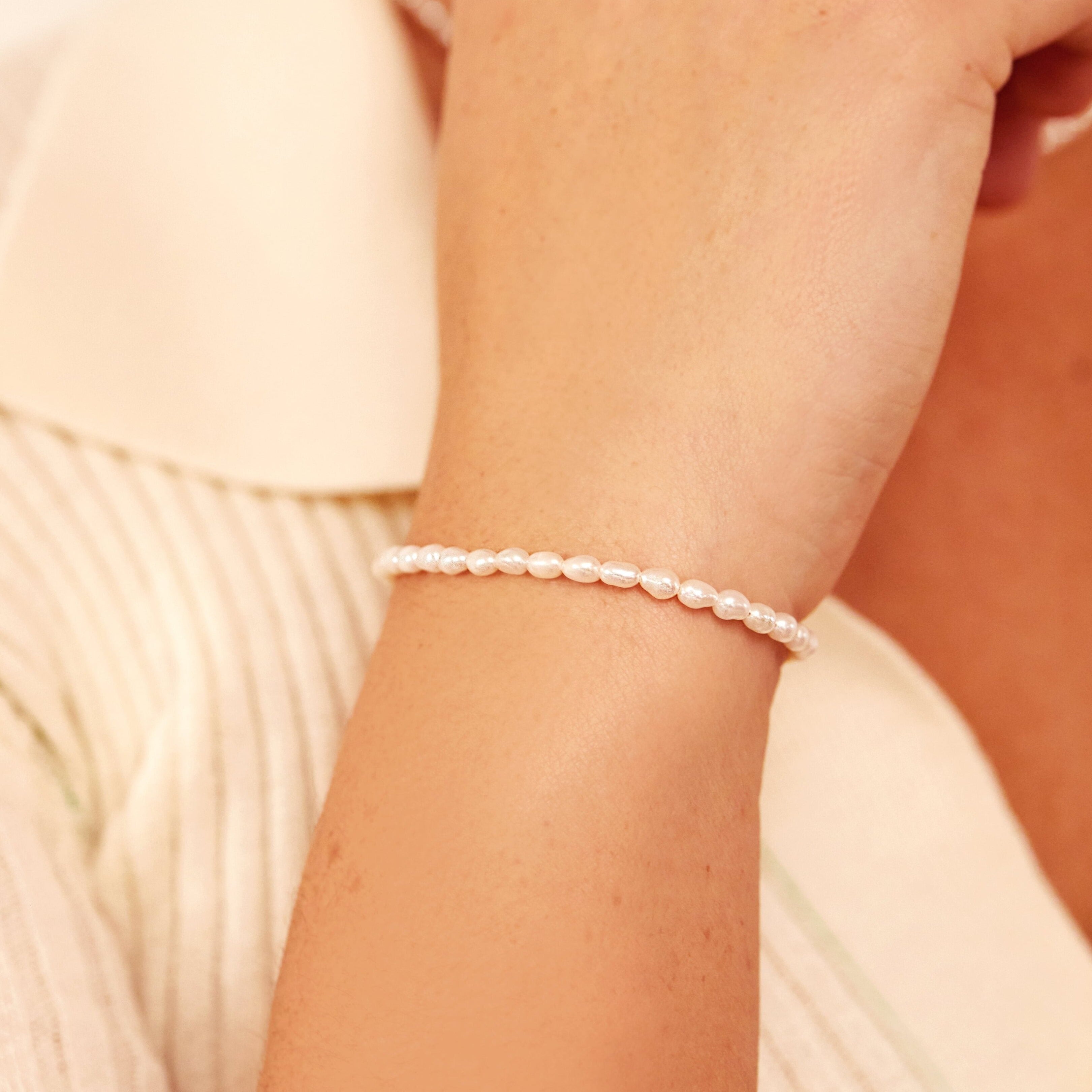 Silver seed pearl bracelet around a wrist of a woman wearing a woollen jumper