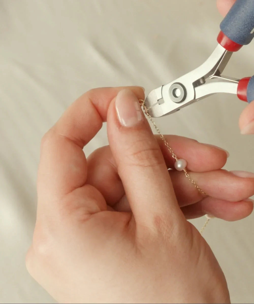 Close-up of a LILY & ROO team member handcrafting a delicate pearl necklace using jewellery pliers in our London studio.