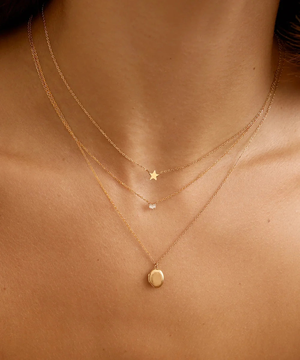 Model wearing three delicate gold necklaces layered at different lengths, featuring a star, diamond and oval pendant.