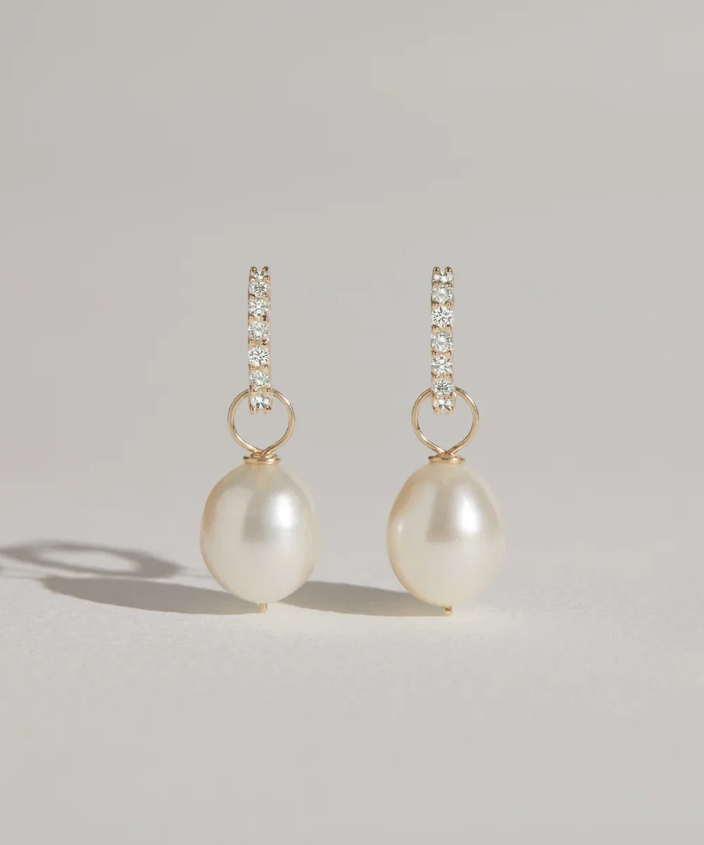 Gold diamond-style huggie hoop earrings with freshwater pearl drops on a neutral background.
