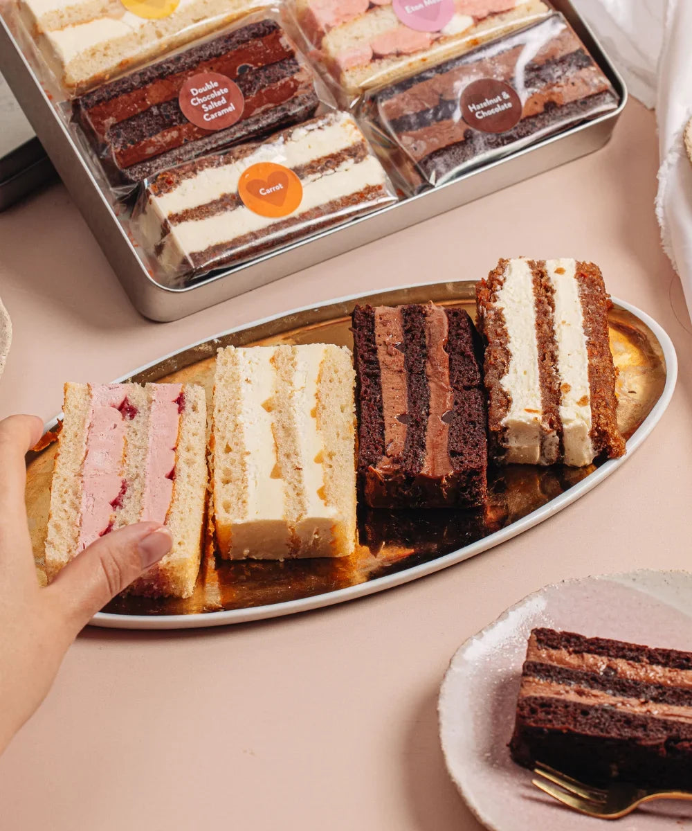 Hand reaching for a slice of cake from a gold platter of wedding cake tasting samples by Cutter & Squidge