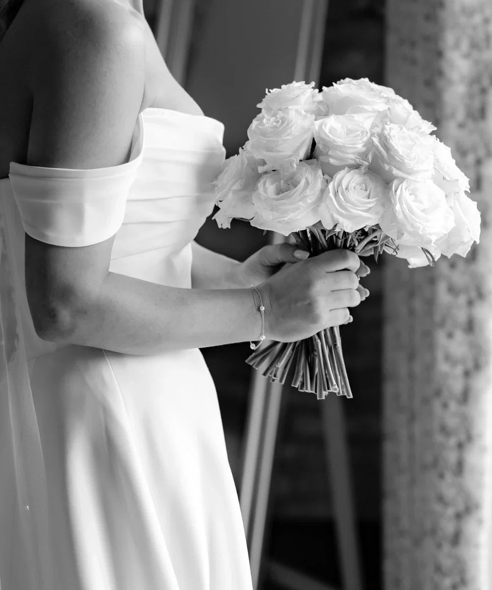 bride holding white rose bouquet wearing delicate pearl bracelet, black and white wedding photography