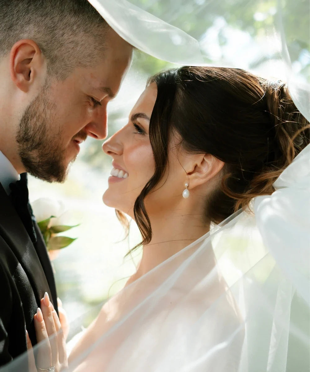 Bride and groom nose-to-nose under wedding veil, bride wearing gold pearl drop earrings