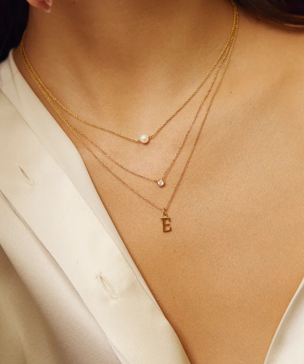 Close-up of layered gold necklaces featuring a single pearl, birthstone pendant and personalised initial necklace.