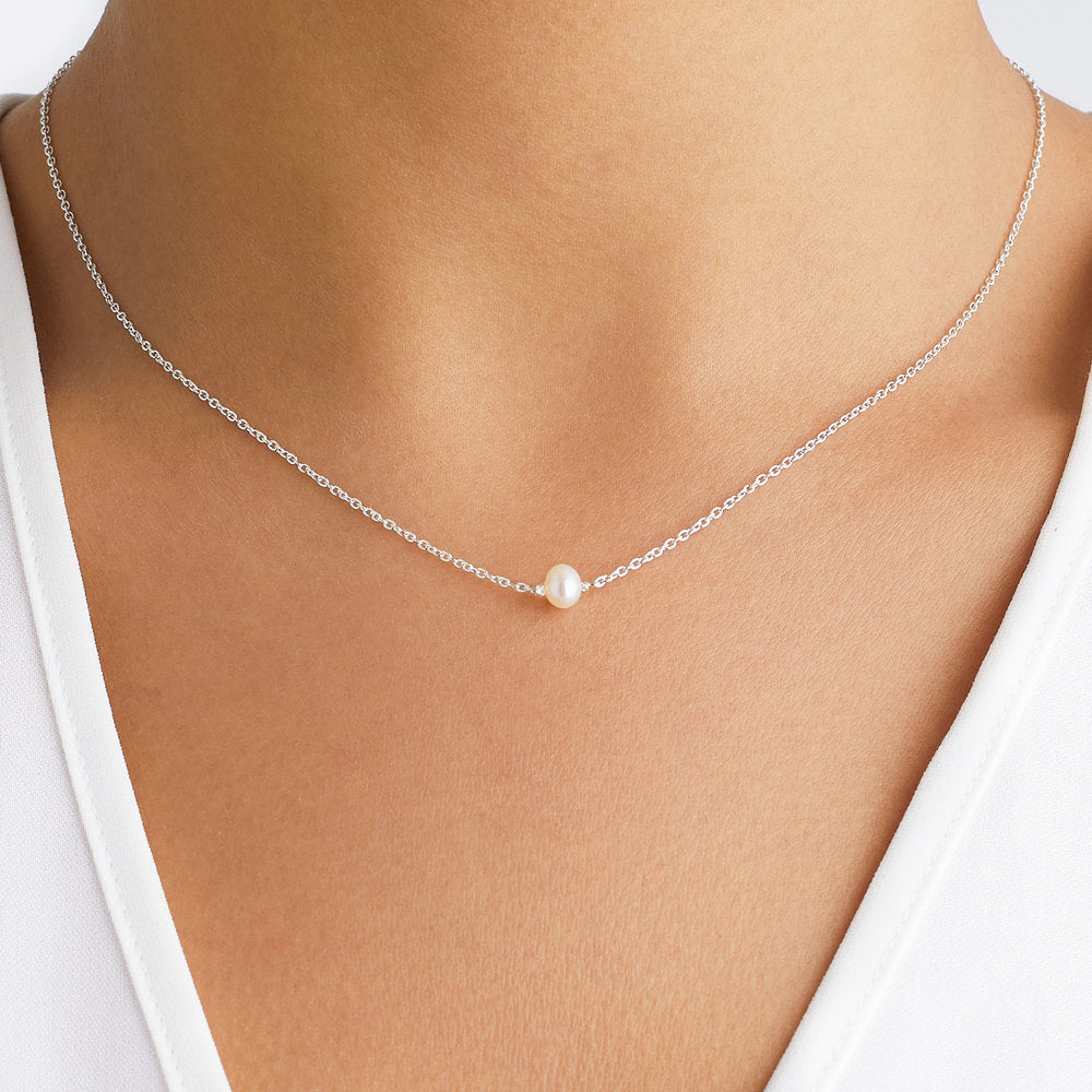 A silver single pearl choker around the neck of a woman wearing a white V-neck top