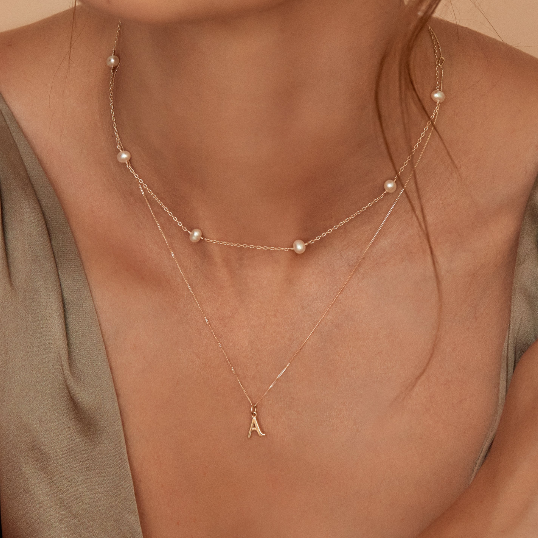 Solid gold curve initial letter necklace 'A' layered with a gold ten pearl choker around a neck
