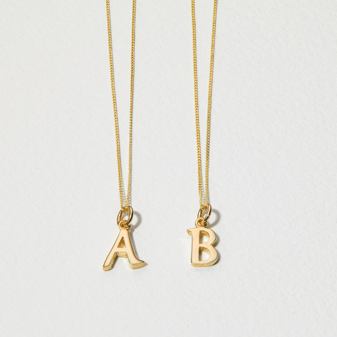 Solid gold curve initial letter necklaces 'A' and 'B' on a paper surface